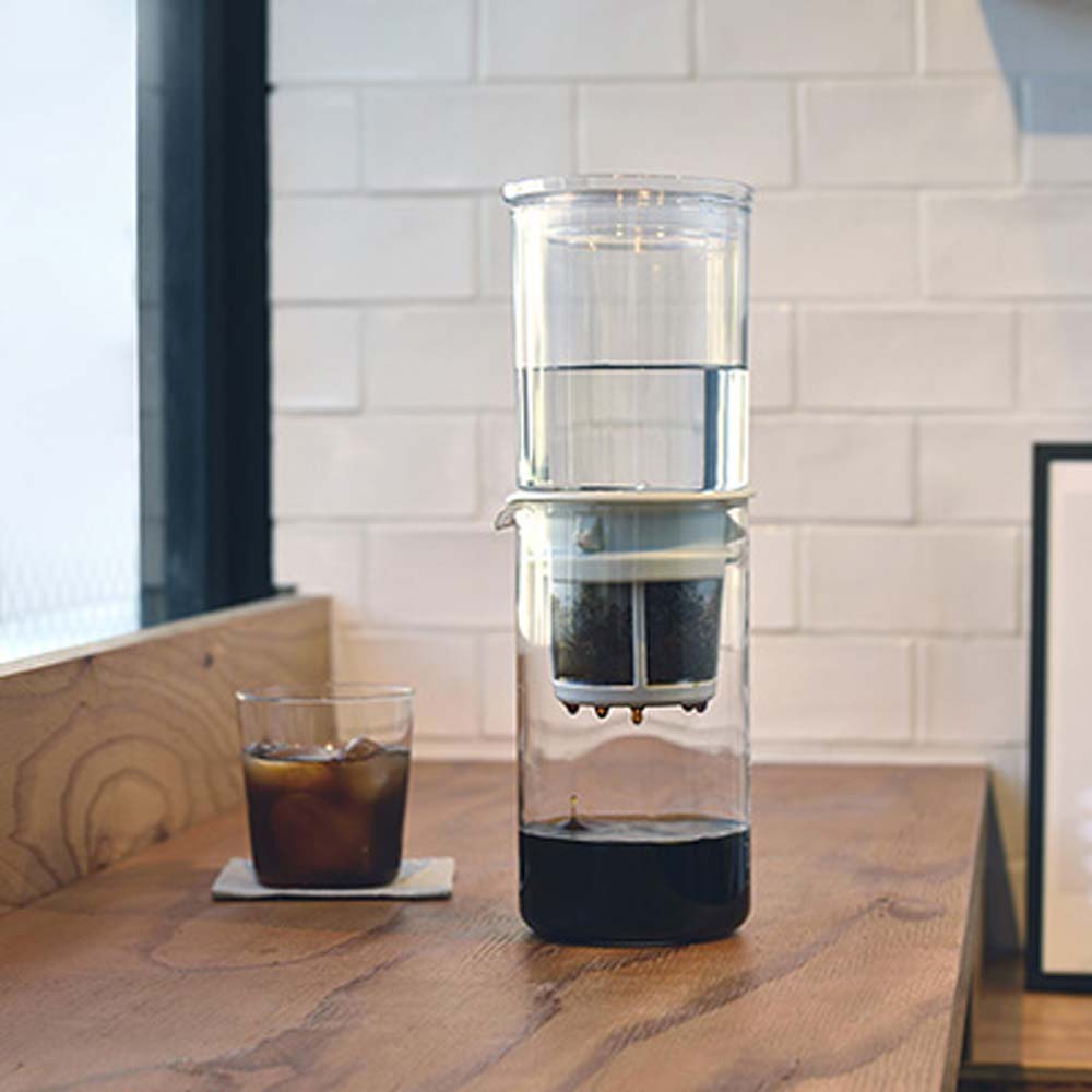 Hario "Drop" Water Dripper, make delicious iced coffee using the natural dripping of water on a table with a cup of brewed ice coffee by side at home.