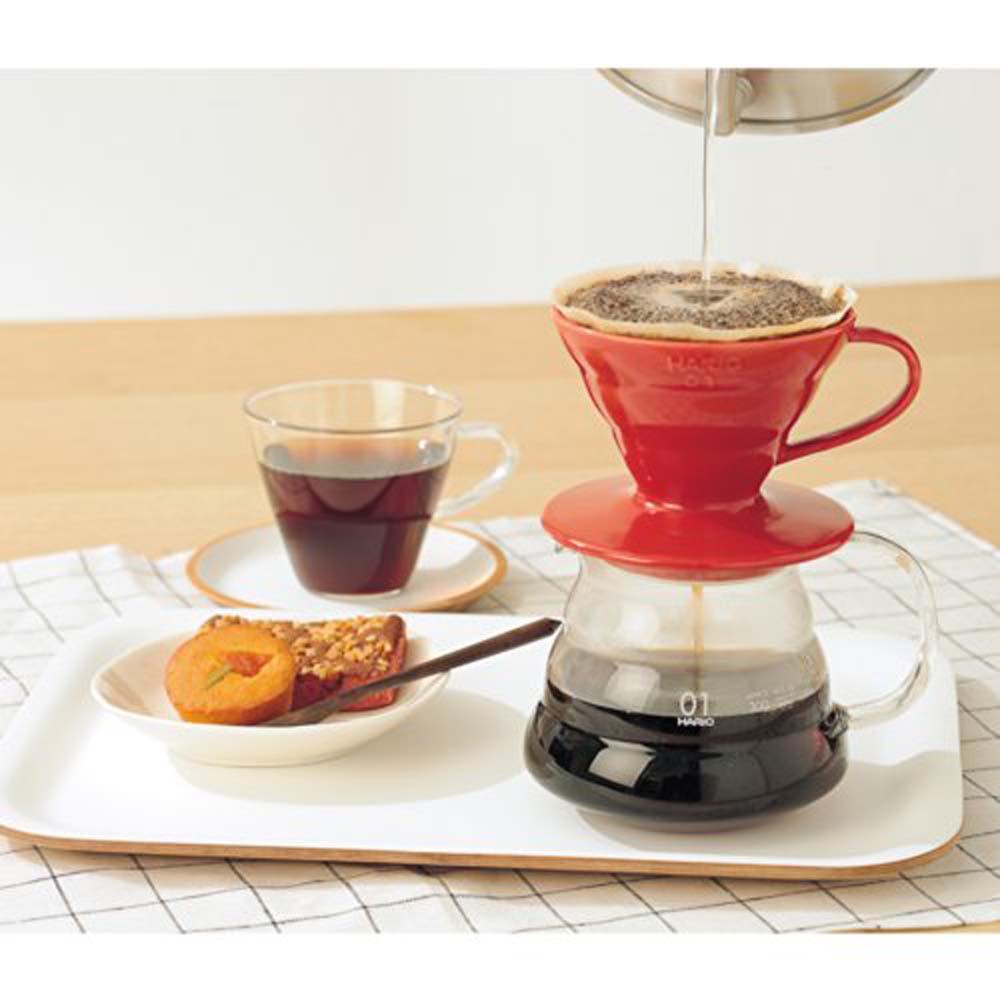 V60 Hario red ceramic dripper. It's exquisite in its design but also effective at what it's meant to do. It shows pour-over brewing with one cup of fresh-brewed coffee and a little plate of cake and fruits.