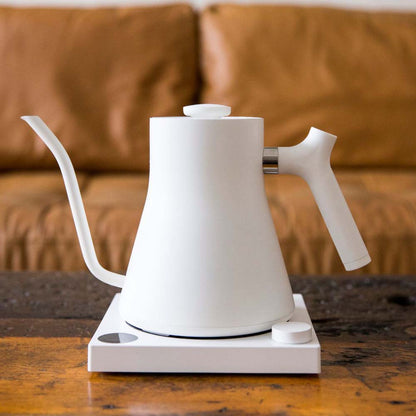 A white Fellow Stagg EKG Electric Kettle on the coffee table front the couch at home.