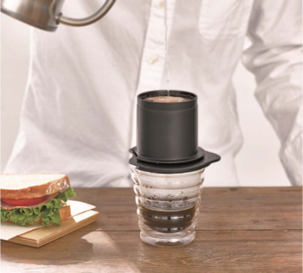 A man brewing coffee from Hario Cafeor Metal Filter Dripper - Black on kitchen bench with home made sanwitch.