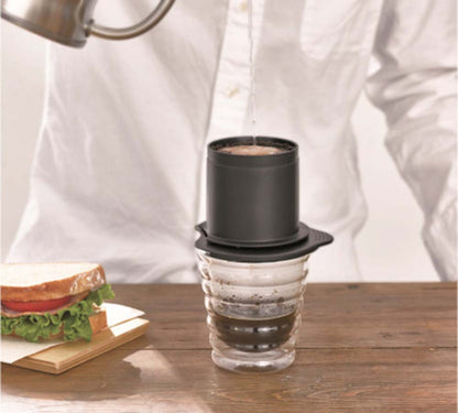 A man brewing coffee from Hario Cafeor Metal Filter Dripper - Black on kitchen bench with home made sanwitch.