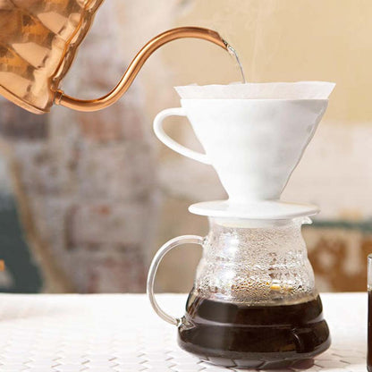 V60 Hario white ceramic dripper. It's exquisite in its design. It shows pour-over brewing with a copper pour-over kettle and v60 glass server.
